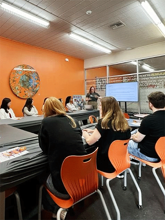 there are many people sitting at a table in a room with orange chairs