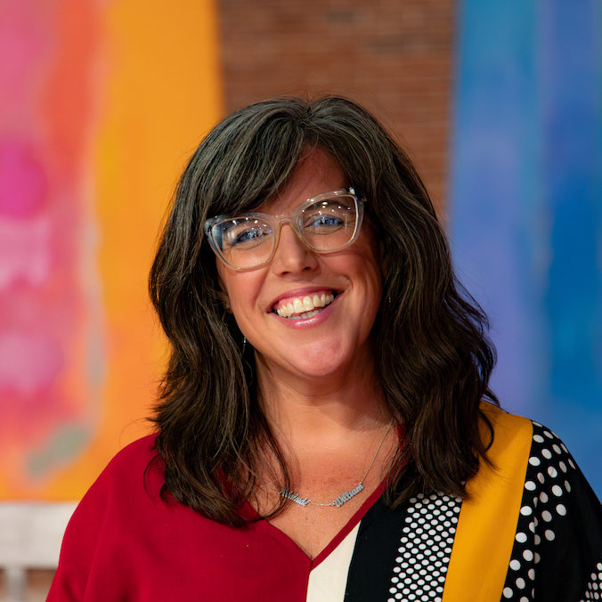 A woman wearing glasses is smiling in front of a colorful background